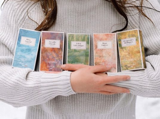 Cô gái mặc áo len xám ôm trọn bộ 5 hộp nước hoa thuần chay Poécile đa dạng mùi hương mang phong cách Pháp.
