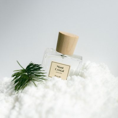 Chai nước hoa thuần chay Poécile Mont Cristal Les Alpes nắp gỗ đặt trên lớp tuyết trắng cùng nhánh thông xanh.
