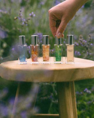 Bàn tay lựa chọn chai nước hoa trong bộ sưu tập Poécile 15ml đặt trên ghế gỗ giữa vườn hoa oải hương cho cung hệ Khí.