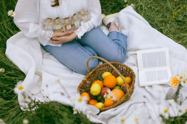 Cô gái ôm trọn bộ sưu tập nước hoa thuần chay Poécile trong buổi dã ngoại bên giỏ trái cây và thảm cỏ xanh.