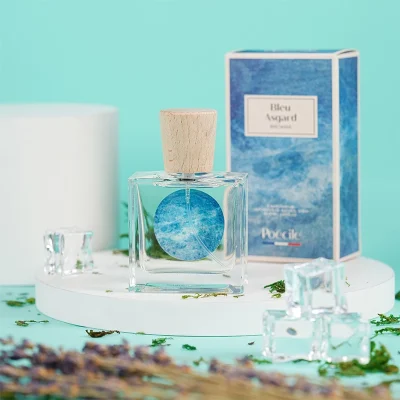 Chai nước hoa thuần chay Poécile Bleu Asgard Bretagne nắp gỗ và vỏ hộp màu xanh biển đặt trên bục tròn cùng đá lạnh.