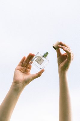 Đôi bàn tay giơ cao mở nắp gỗ chai nước hoa thuần chay Poécile Bleu Asgard Bretagne hướng về bầu trời sáng trong.