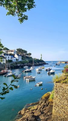 Vịnh biển yên bình vùng Bretagne nước Pháp với thuyền buồm neo đậu trên làn nước xanh ngắt và ngọn hải đăng xa xa.   