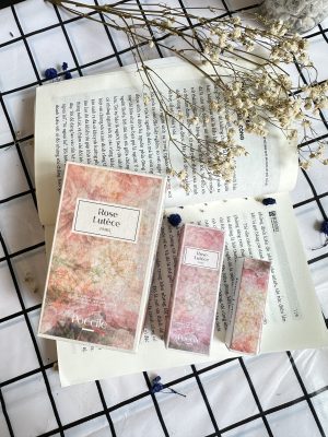 Bộ ba hộp nước hoa Poécile Rose Lutèce Paris các dung tích 50ml, 15ml và mẫu thử trên trang sách mở cùng hoa khô mộc mạc.   
